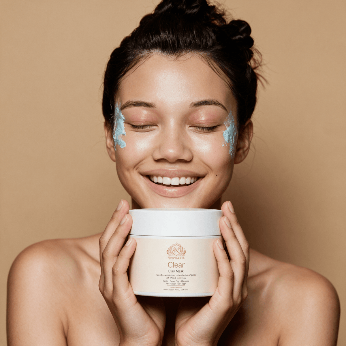Clay Mask for Pores in a white cosmetic jar, held by a smiling woman wearing blue clay mask on her cheeks