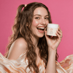 Face and Body Scrub in a white cream jar with a pale peach label, held beside a smiling woman