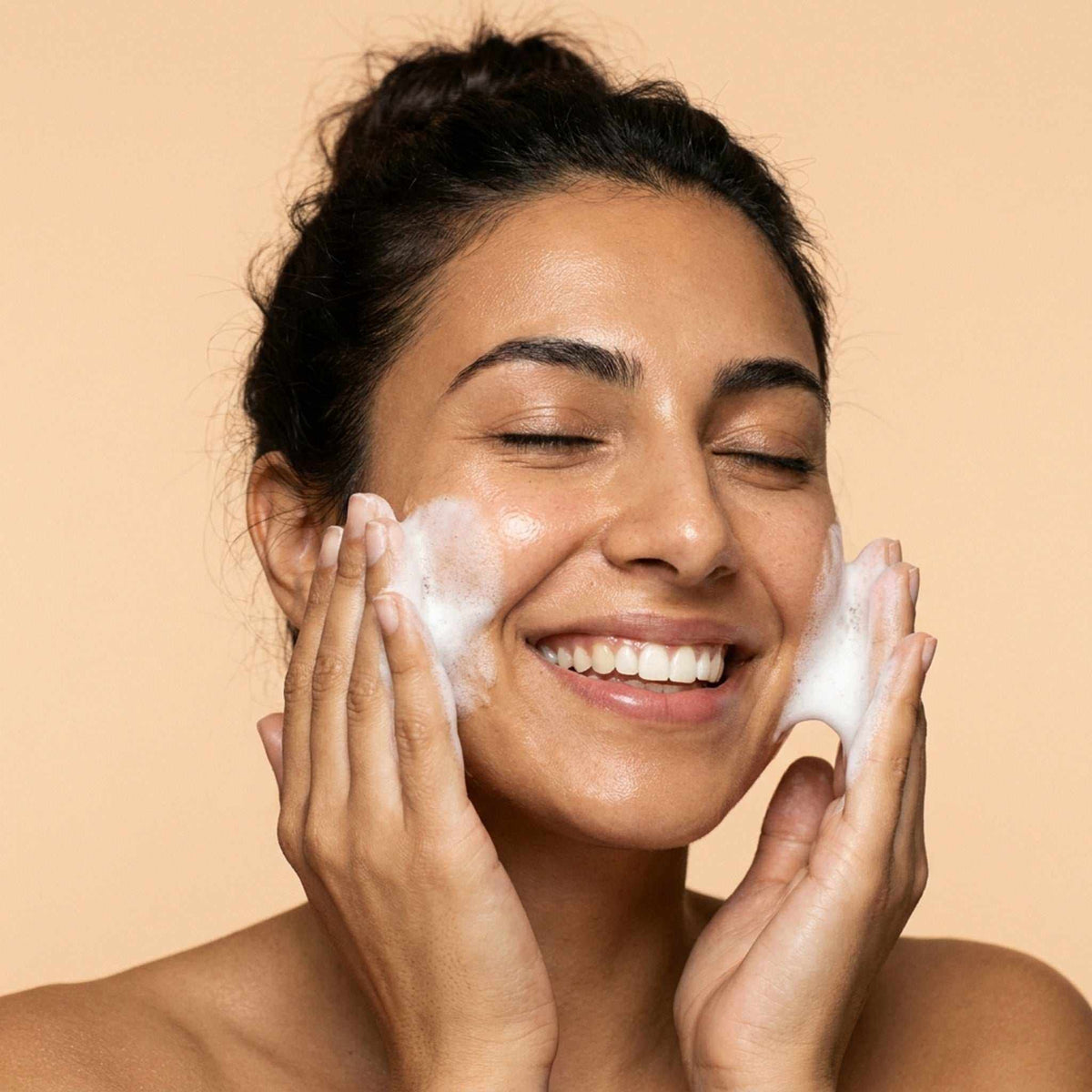 Foam Cleanser for Oily Skin shown as white foamy lather massaged onto a smiling woman’s cheeks with both hands