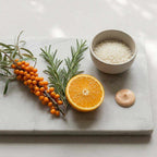 Kojic Acid Cream shown as a smooth beige dollop beside orange, sea buckthorn berries, rosemary and rice