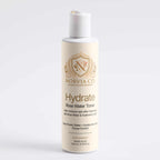 A bottle of Norvia Co. Hydrate Rose Water Toner with a white cap and cream-colored body, featuring gold lettering and a crest logo, set against a plain light gray background.