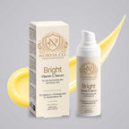 Vitamin C Serum in a white bottle with gold branding beside a matching cream box, featuring a gold botanical emblem