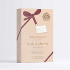 A beige rectangular gift box for The Apothecary's Daily Radiance Holiday Edition 2016, decorated with a dark burgundy ribbon graphic and a white gift tag, set against a clean white background.